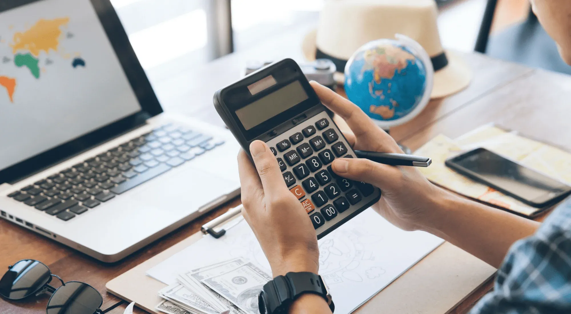 Digital nomad using a calculator with a laptop, money and world map in the background