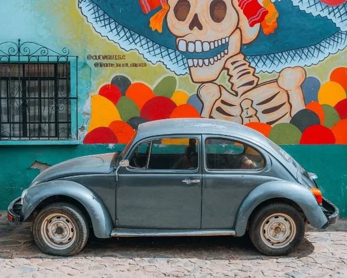 Vintage car parked in front of a murales in Oaxaca