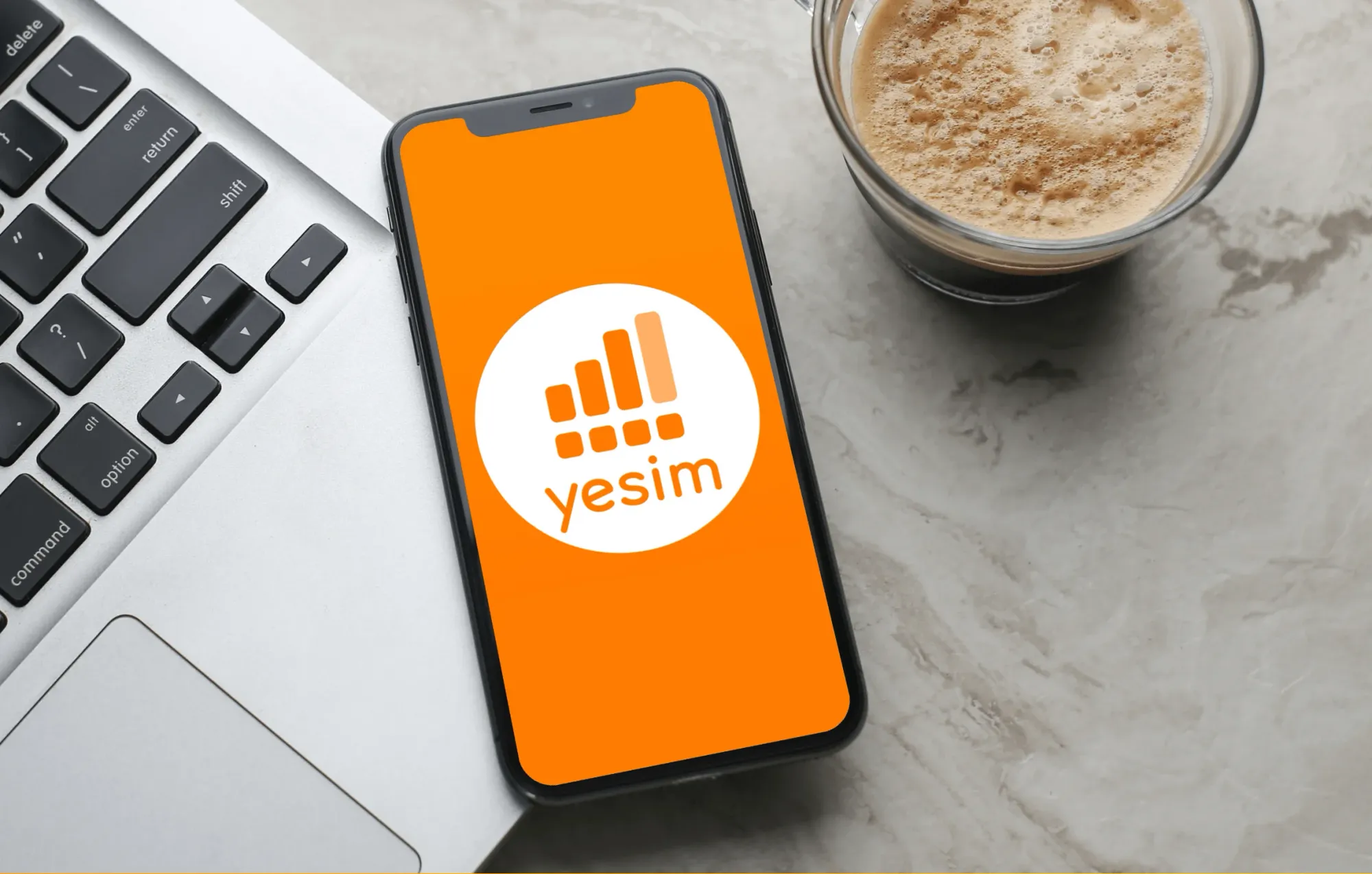 Yesim app on a phone next to a laptop and coffee cup