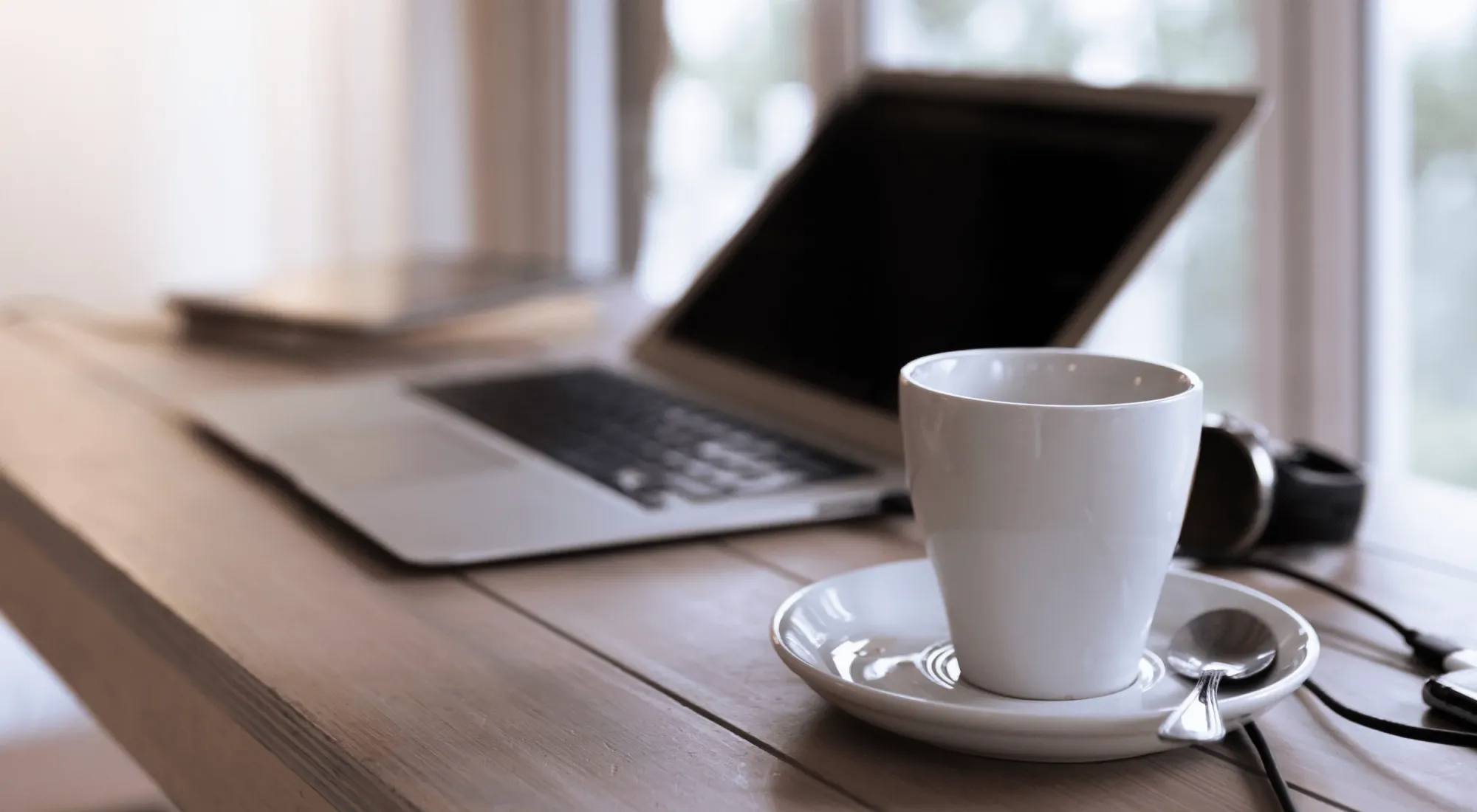 Laptop next to cup of coffee on a wooden table top in a cafe