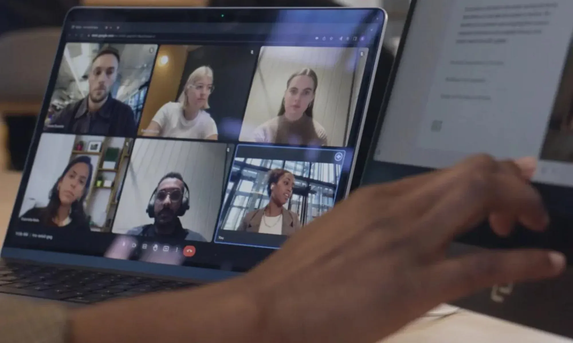 a person taking notes while looking at a conference call on a second monitor 