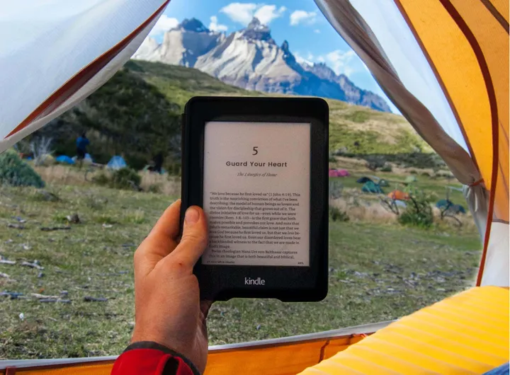 Man reading a digital nomad book from a Kindle while camping