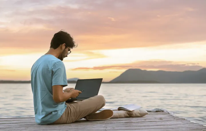 Digital nomad connecting to the Wi-Fi with his laptop in front of a lake at sunset